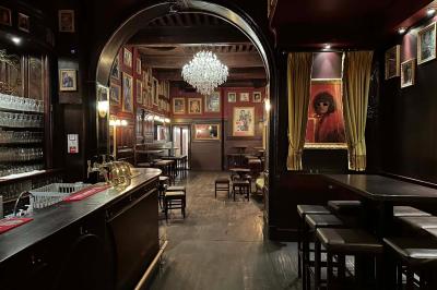Intérieur d'un bar avec un lustre central, des murs ornés de cadres et un comptoir en bois sombre.
