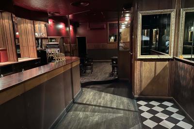 Intérieur d'un bar avec un lustre central, des murs ornés de cadres et un comptoir en bois sombre.