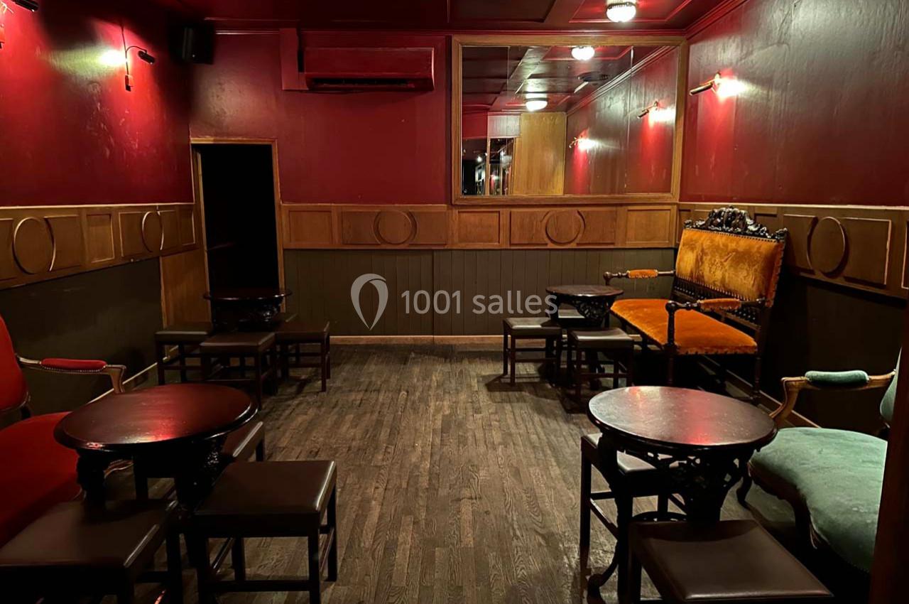 Salle intimiste avec murs rouges, mobilier en bois sombre, fauteuils colorés et éclairage tamisé.