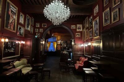 Intérieur d'un bar avec un lustre central, des murs ornés de cadres et un comptoir en bois sombre.