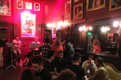 Intérieur d'un bar avec un lustre central, des murs ornés de cadres et un comptoir en bois sombre.