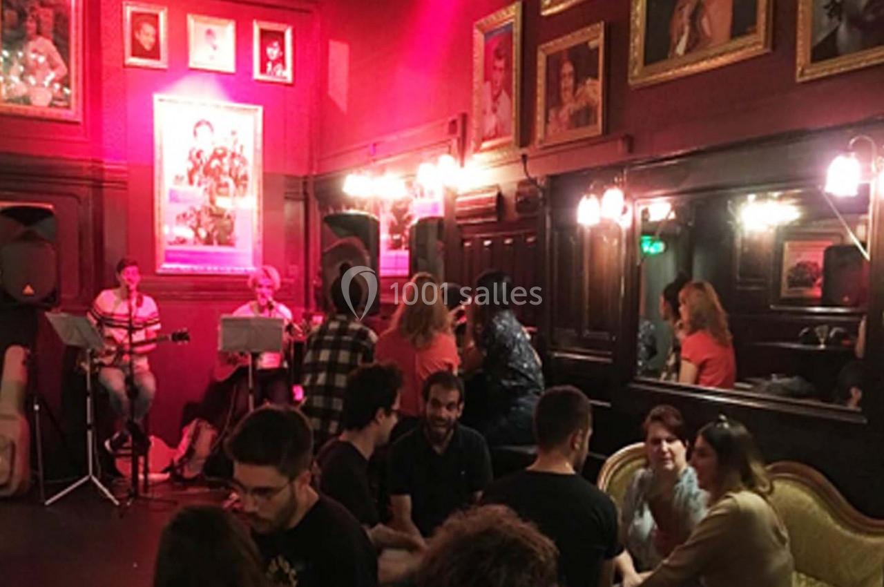 Des personnes discutent dans un café à l'ambiance chaleureuse, avec des musiciens jouant en arrière-plan.