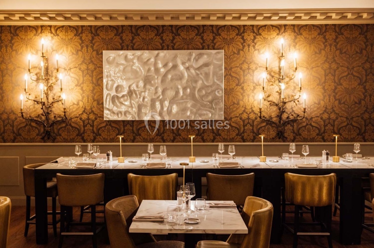 Salle de restaurant élégante avec tables dressées, chaises en velours, éclairage chaleureux et décoration murale raffinée.