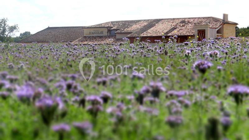 Champ de fleurs violettes floues au premier plan avec un bâtiment en pierre et toit en tuiles en arrière-plan.