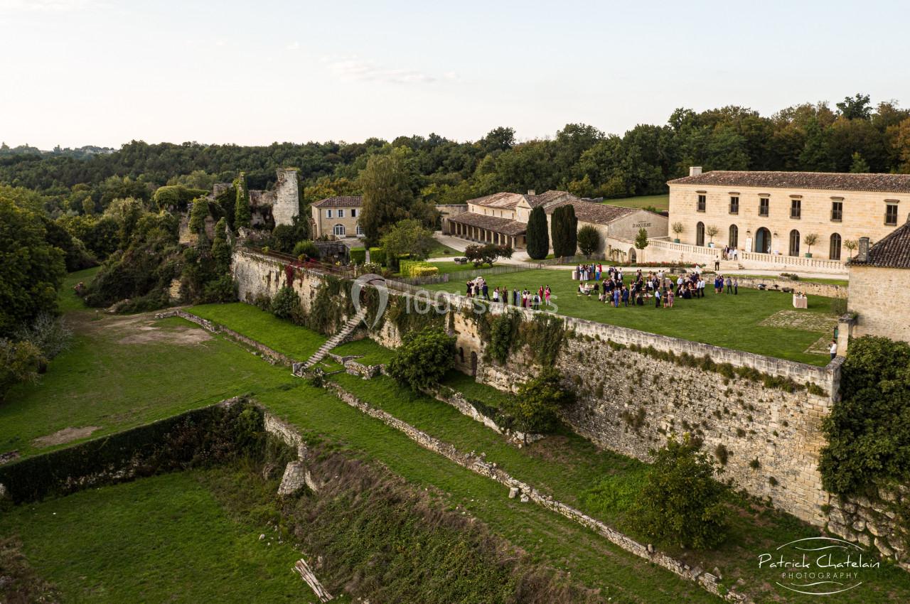 Vue aérienne d'un château entouré de verdure, avec un rassemblement de personnes dans la cour principale.
