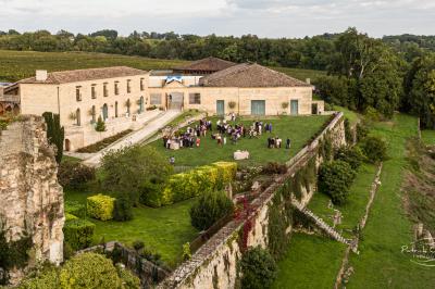 Vue aérienne d'un domaine entouré de vignes, de bâtiments en pierre et d'un cours d'eau bordé de verdure.