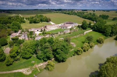 Vue aérienne d'un domaine entouré de vignes, de bâtiments en pierre et d'un cours d'eau bordé de verdure.