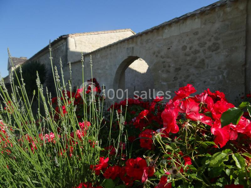 Mur en pierre avec une arche, entouré de lavandes et de fleurs rouges sous un ciel bleu clair.