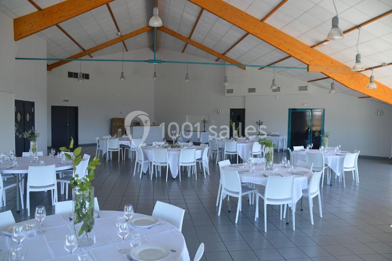 Salle de réception lumineuse avec tables rondes dressées de nappes blanches, chaises modernes et décoration sobre.