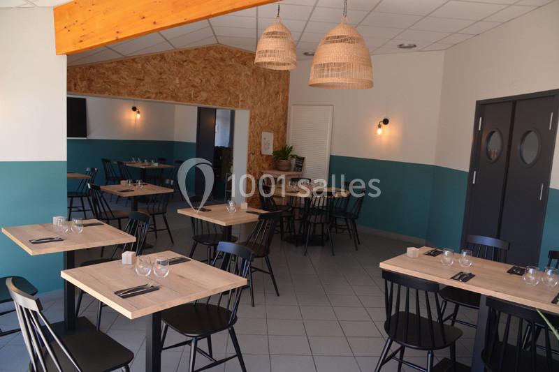 Salle de restaurant moderne avec tables en bois clair, chaises noires et luminaires en osier suspendus.