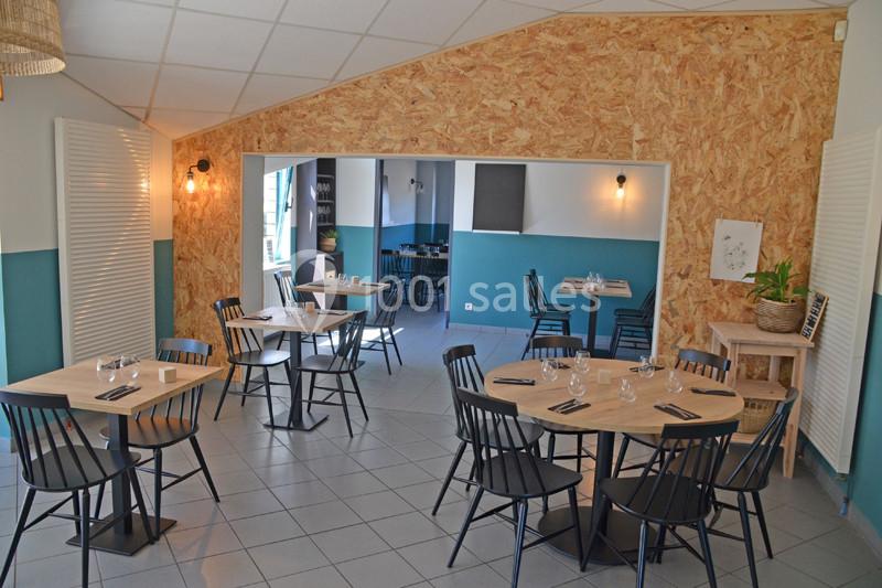 Salle de restaurant lumineuse avec tables en bois, chaises noires et murs bleu et bois clair.