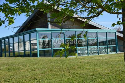 Pelouse verdoyante avec un grand arbre, bâtiment moderne en arrière-plan et ciel dégagé.