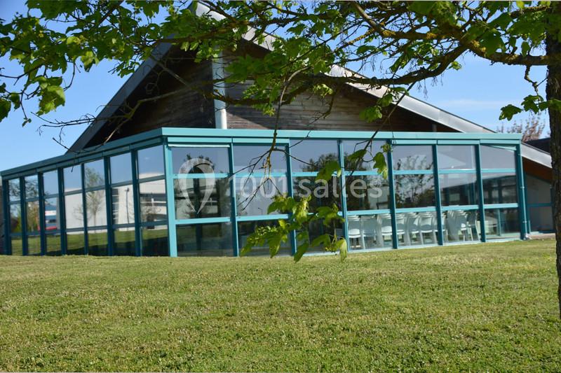 Bâtiment moderne avec une façade vitrée donnant sur une pelouse, partiellement ombragée par des branches d'arbre.