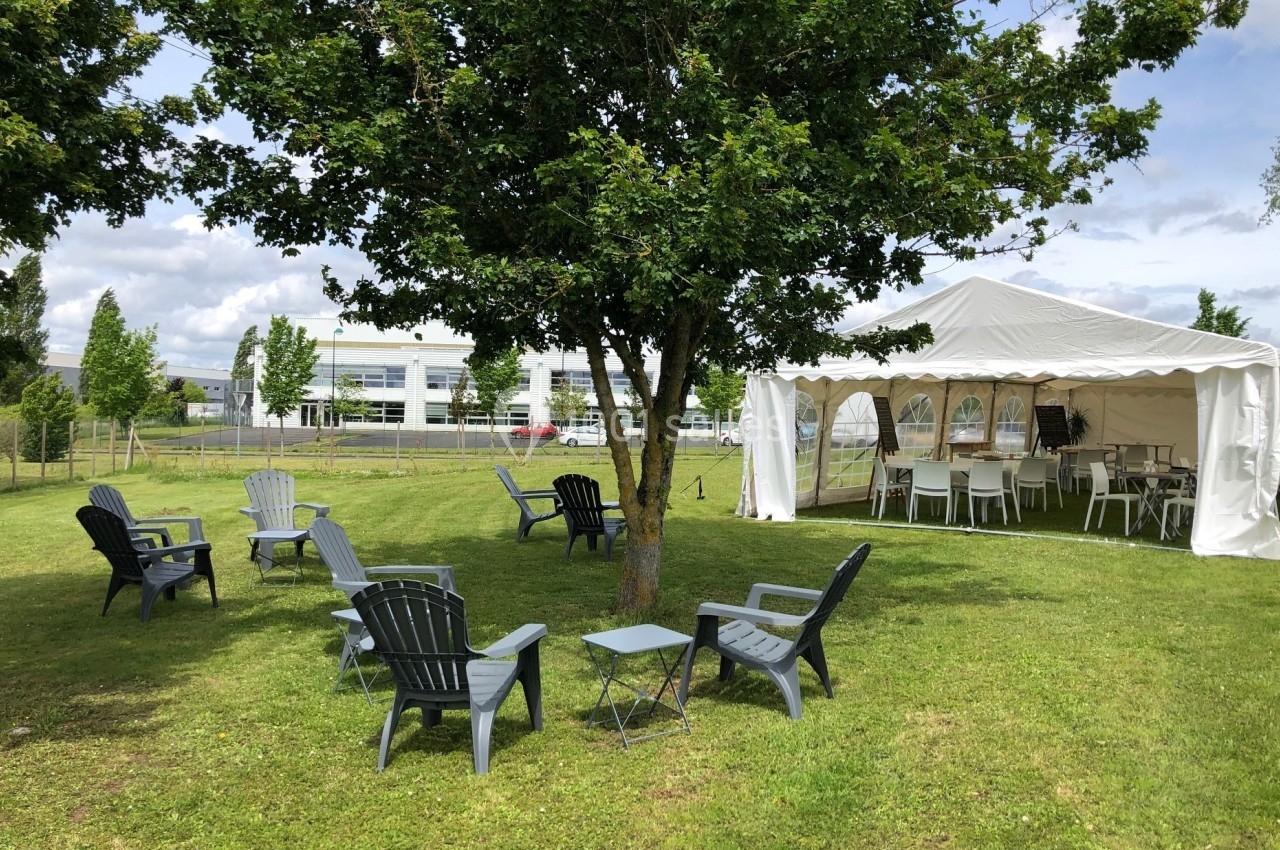 Chaises disposées autour d'un arbre sur une pelouse, avec une tente blanche aménagée en arrière-plan.