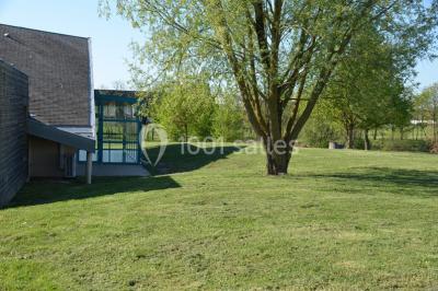 Pelouse verdoyante avec un grand arbre, bâtiment moderne en arrière-plan et ciel dégagé.