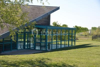 Pelouse verdoyante avec un grand arbre, bâtiment moderne en arrière-plan et ciel dégagé.