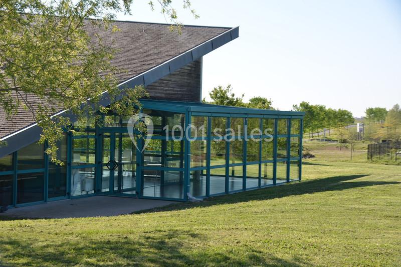 Bâtiment moderne avec façade en verre, entouré de pelouse et d'arbres sous un ciel dégagé.