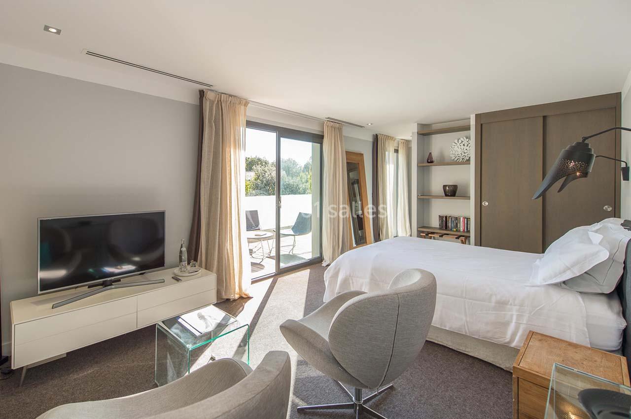 Chambre lumineuse avec lit double, fauteuils, télévision, grande baie vitrée donnant sur une terrasse extérieure.