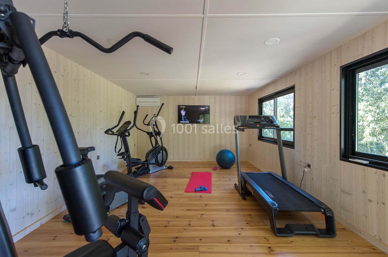 Salle de sport lumineuse avec tapis de course, vélos d'exercice, ballon, tapis de yoga et écran mural.