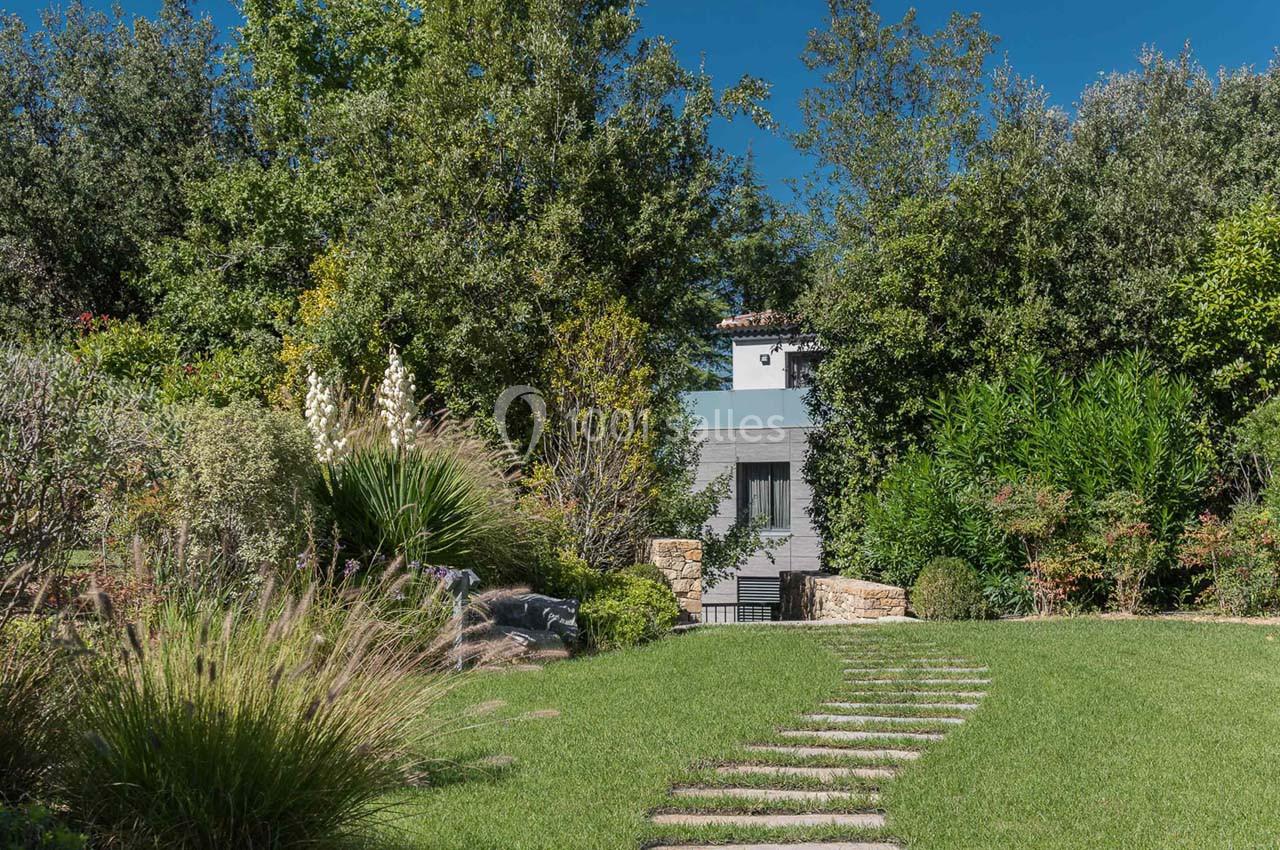 Chemin en pierre menant à une maison moderne entourée de végétation dense et d'un jardin verdoyant.