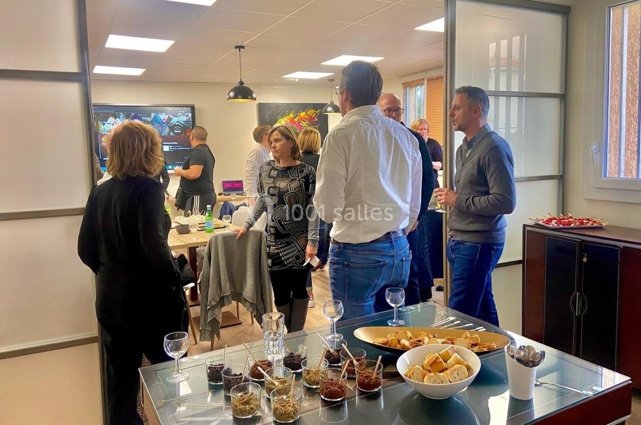 Groupe de personnes discutant dans une salle lumineuse avec des tables garnies de snacks et de boissons.