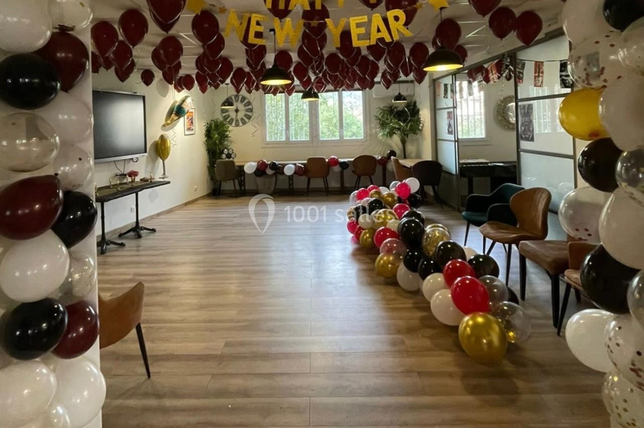 Salle décorée pour le Nouvel An avec des ballons colorés, une bannière ’Happy New Year’ et des chaises disposées autour.