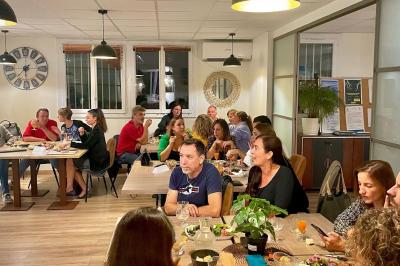 Des personnes assises autour de tables dans une salle lumineuse, partageant un repas ou discutant.