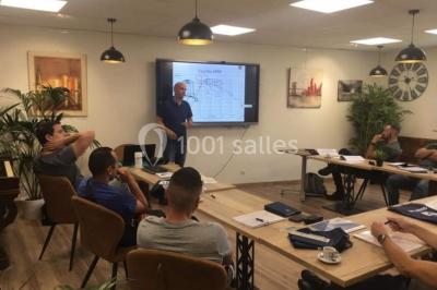 Miniature Location salle La Garde (Var) - City Var #4 Salle de réunion lumineuse avec plusieurs tables, chaises variées, plantes vertes et un écran mural.