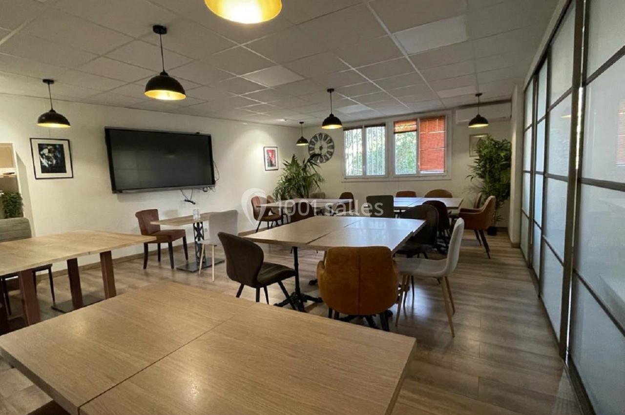 Salle de réunion lumineuse avec tables en bois, chaises variées, écran mural et plantes décoratives.