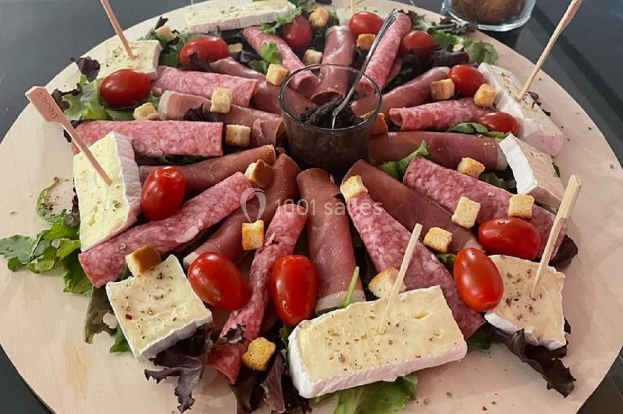 Plateau circulaire de charcuterie et fromage avec tomates cerises, croûtons et salade, disposé autour d'une sauce centrale.