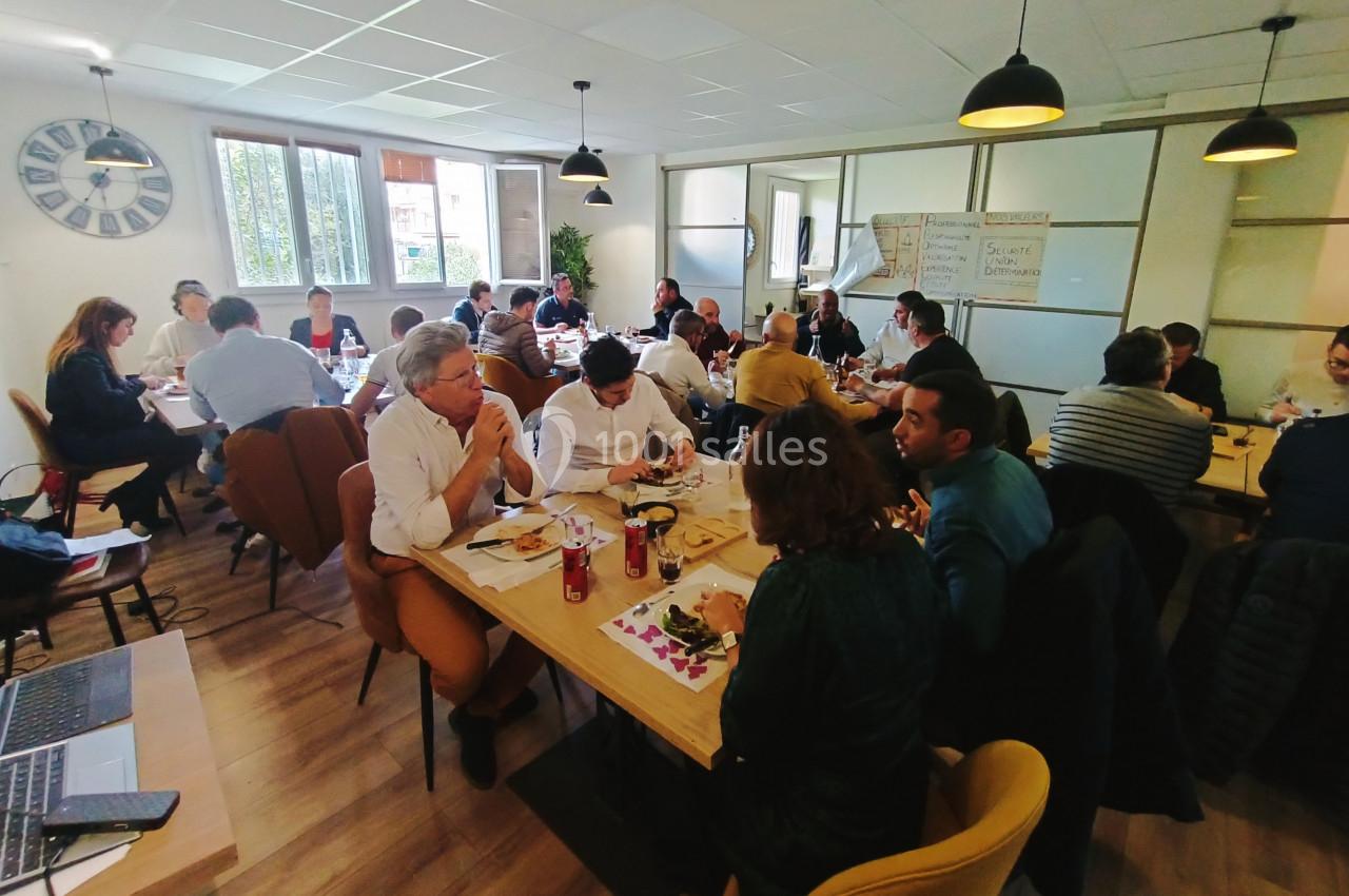 Des personnes assises autour de tables dans une salle lumineuse, participant à une réunion ou un atelier collaboratif.