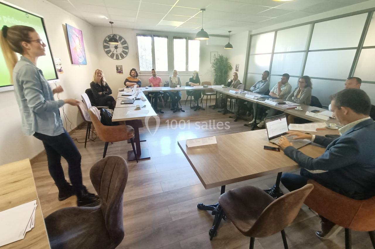 Une femme présente devant un groupe de personnes assises autour de tables dans une salle de réunion lumineuse.