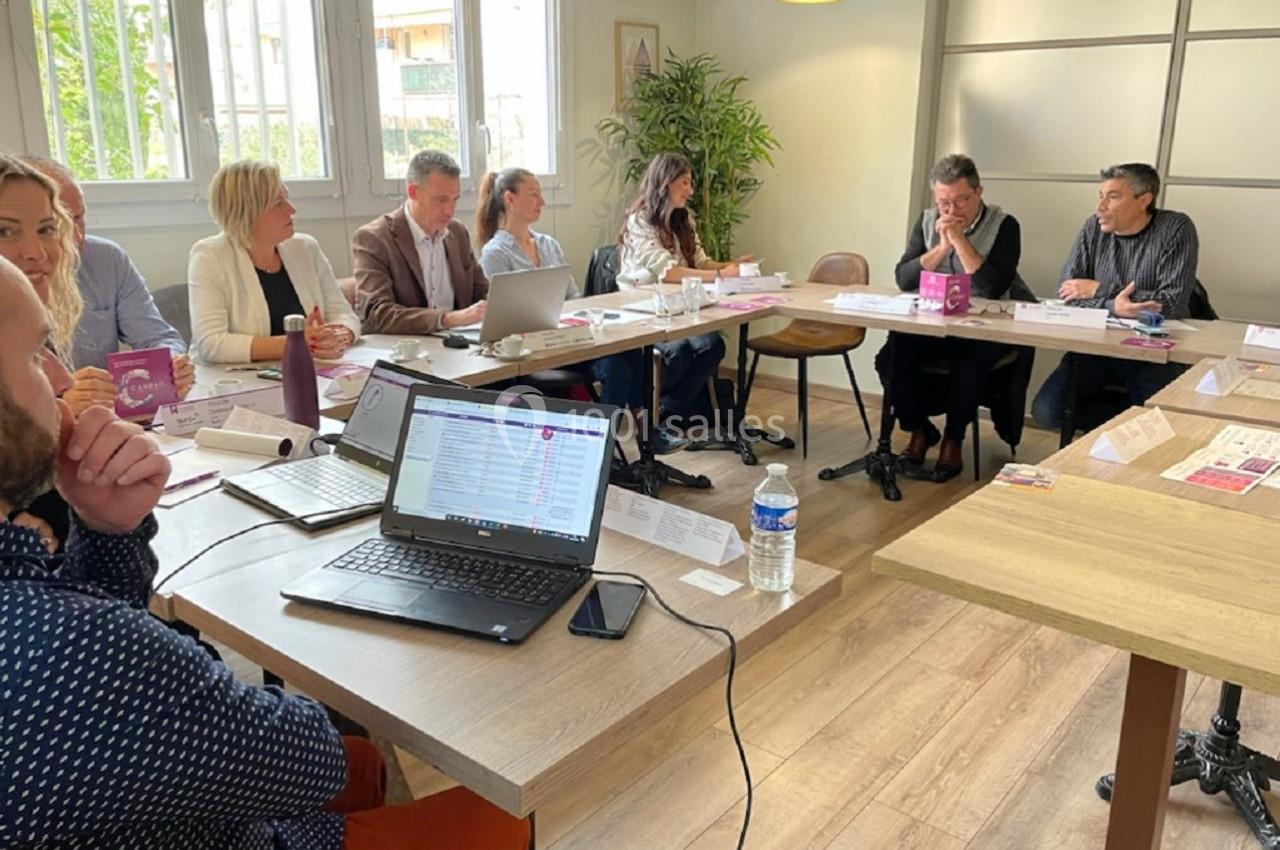 Des personnes participent à une réunion autour de tables, avec des ordinateurs portables et des documents.