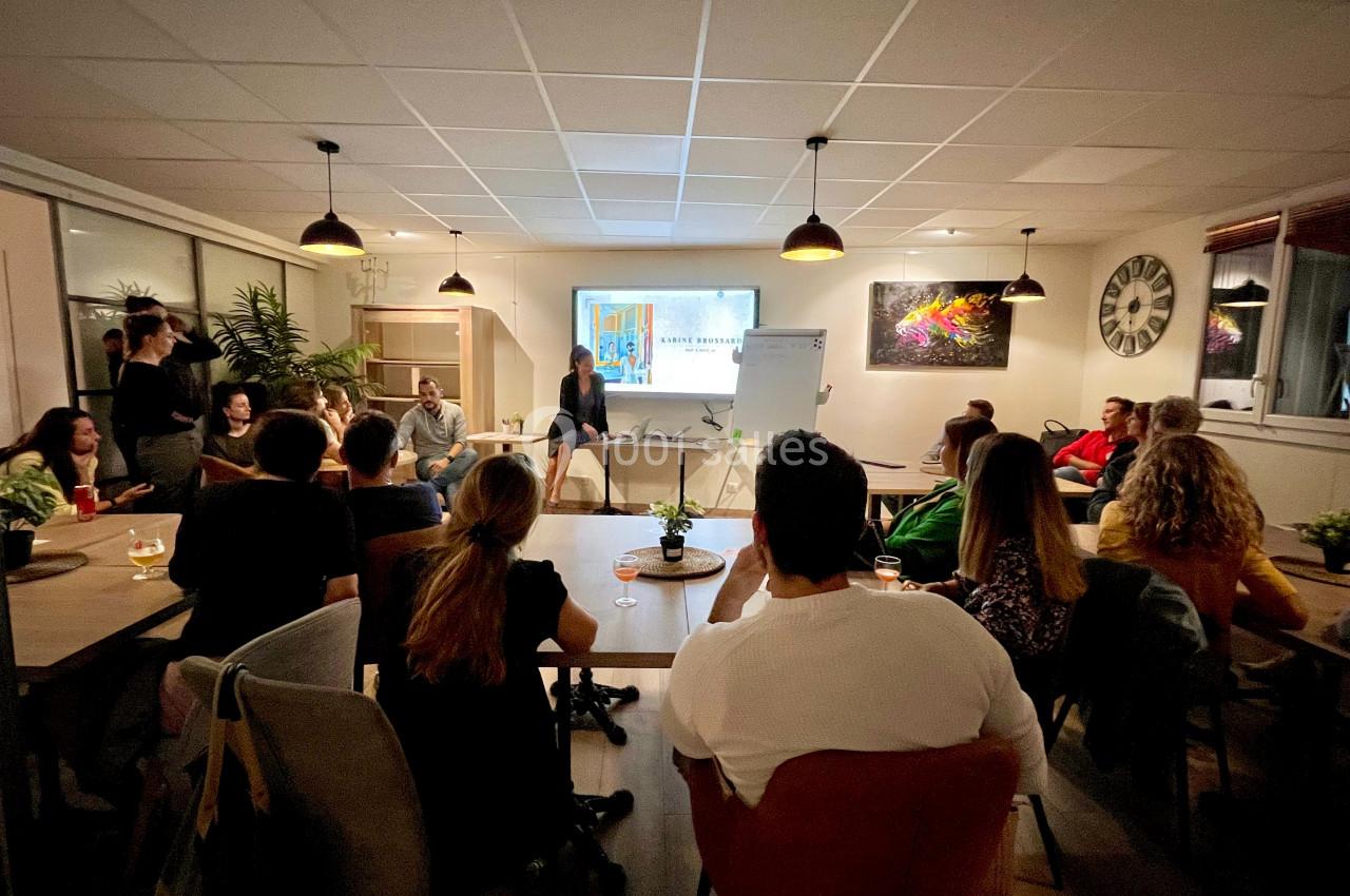 Groupe de personnes assises dans une salle, écoutant une présentation projetée sur un écran.