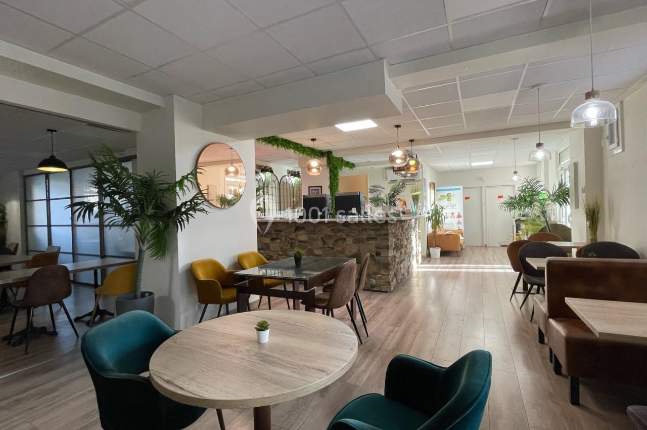 Salle lumineuse avec tables en bois, chaises colorées, plantes décoratives et comptoir en pierre au fond.