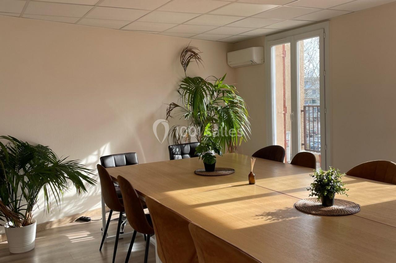Salle de réunion lumineuse avec une grande table en bois, des chaises en cuir et des plantes décoratives.