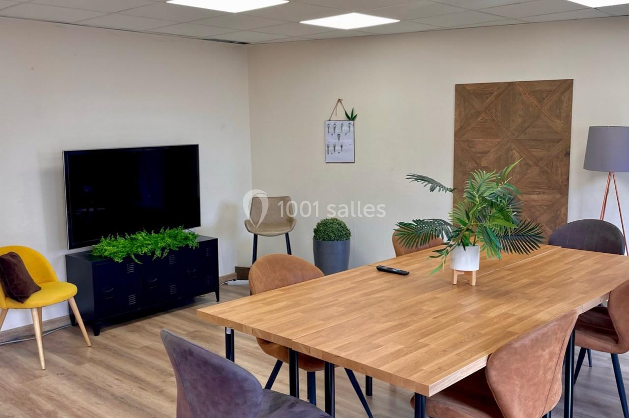 Salle de réunion lumineuse avec table en bois, chaises colorées, plantes décoratives et écran mural.
