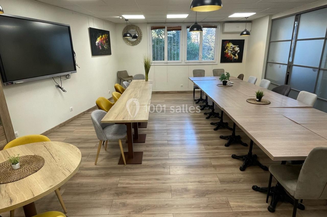 Salle de réunion lumineuse avec tables en bois, chaises colorées, écran mural et grandes fenêtres donnant sur l'extérieur.
