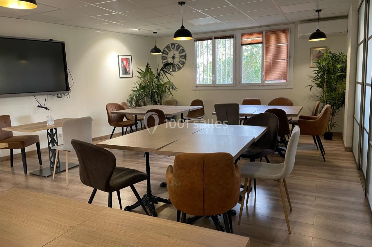 Salle de réunion lumineuse avec plusieurs tables, chaises variées, plantes vertes et un écran mural.