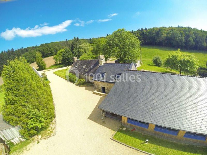 Vue aérienne d'un ensemble de bâtiments en pierre avec toitures en ardoise, entouré de verdure et d'allées gravillonnées.