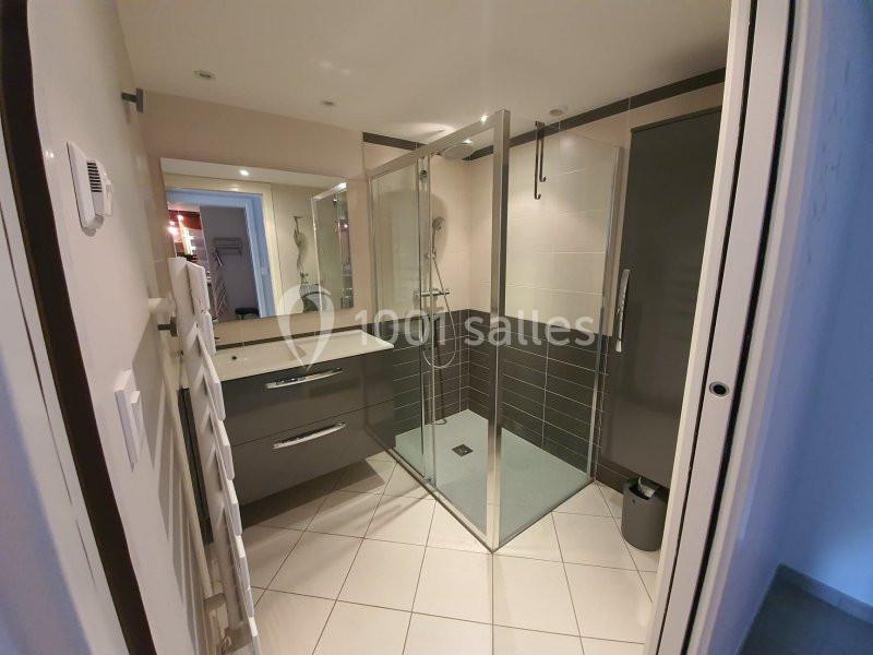 Salle de bain moderne avec douche à paroi vitrée, meuble vasque gris et carrelage clair au sol.