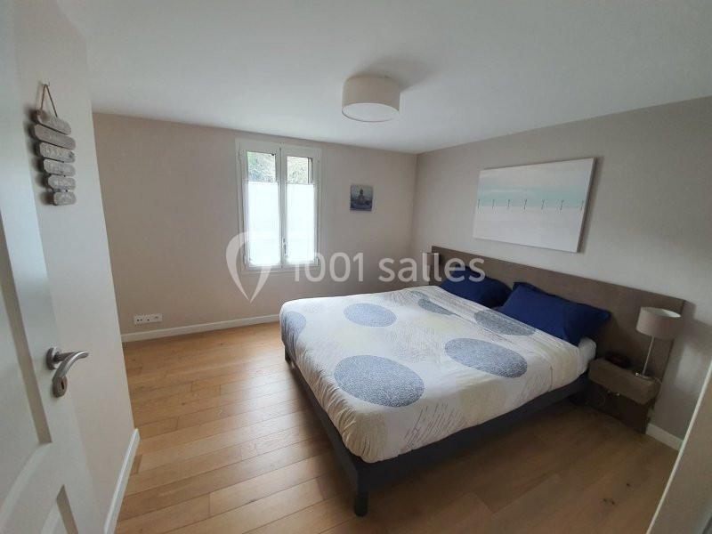 Chambre lumineuse avec lit double, parure à motifs bleus, parquet en bois clair et mur décoré de tableaux.