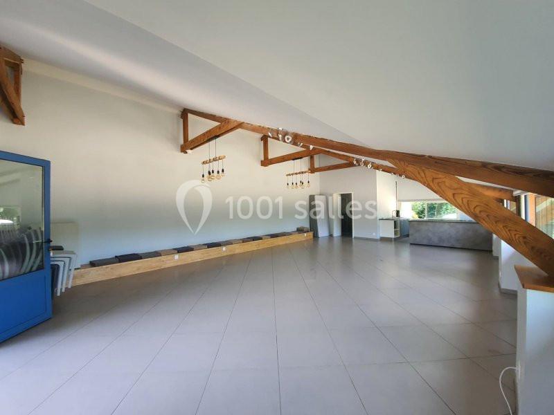 Salle lumineuse avec poutres apparentes, carrelage clair, grandes fenêtres et mobilier minimaliste.