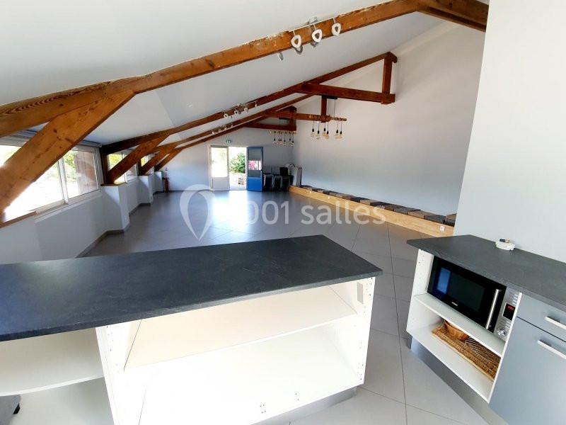 Vue d'une grande pièce lumineuse avec poutres apparentes, cuisine ouverte et espace aménageable au fond.