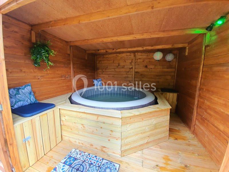 Jacuzzi gonflable installé dans un abri en bois avec coussins, plantes décoratives et éclairage.