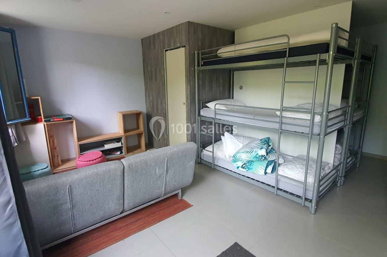 Chambre avec lits superposés, canapé gris, étagères en bois et lumière naturelle entrant par une fenêtre.