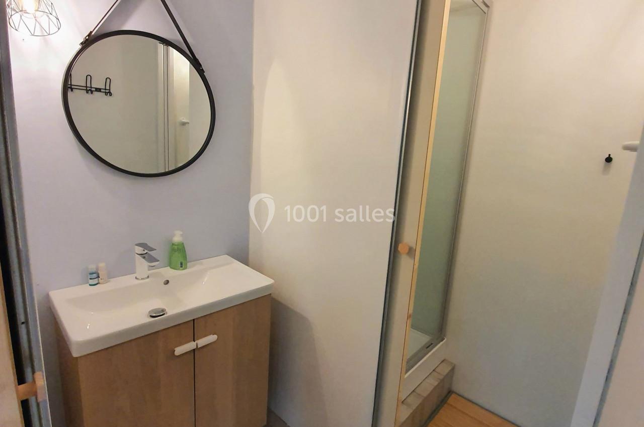Salle de bain avec lavabo sur meuble en bois, miroir rond mural, et douche avec porte coulissante.