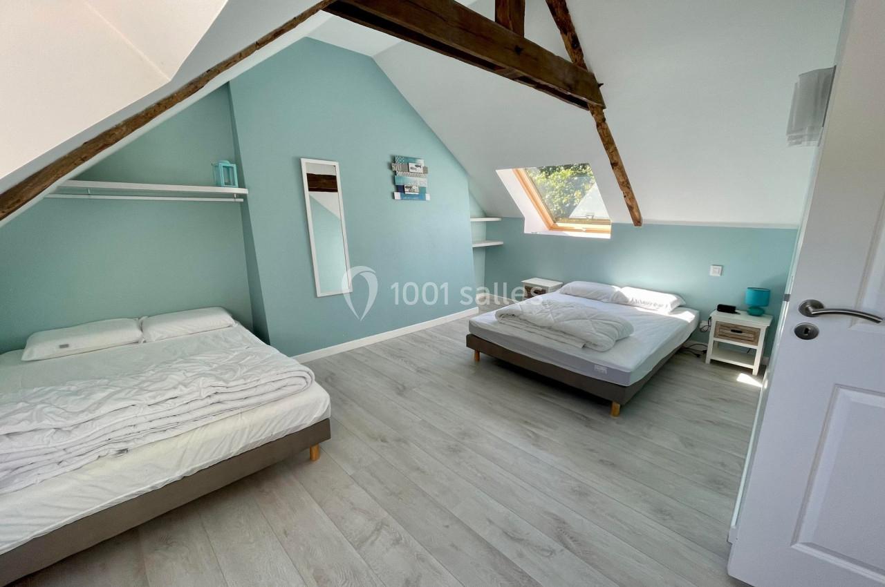 Chambre mansardée avec deux lits doubles, poutres apparentes, murs verts et fenêtre de toit laissant entrer la lumière.