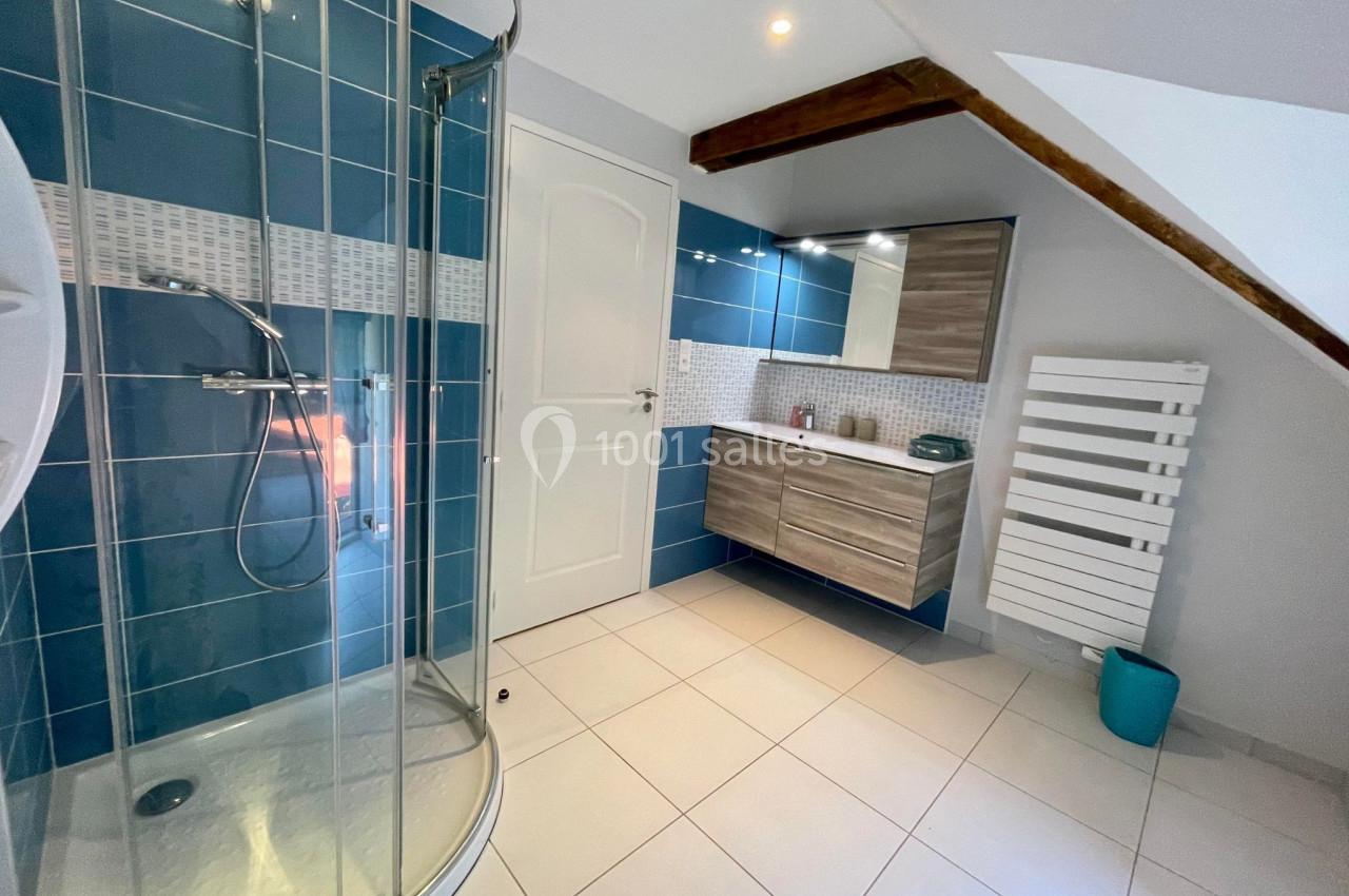 Salle de bain moderne avec douche arrondie, carrelage bleu et blanc, meuble en bois et radiateur mural.