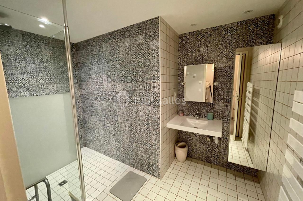 Salle de bain avec douche à l'italienne, murs en carreaux à motifs, lavabo suspendu et miroir éclairé.